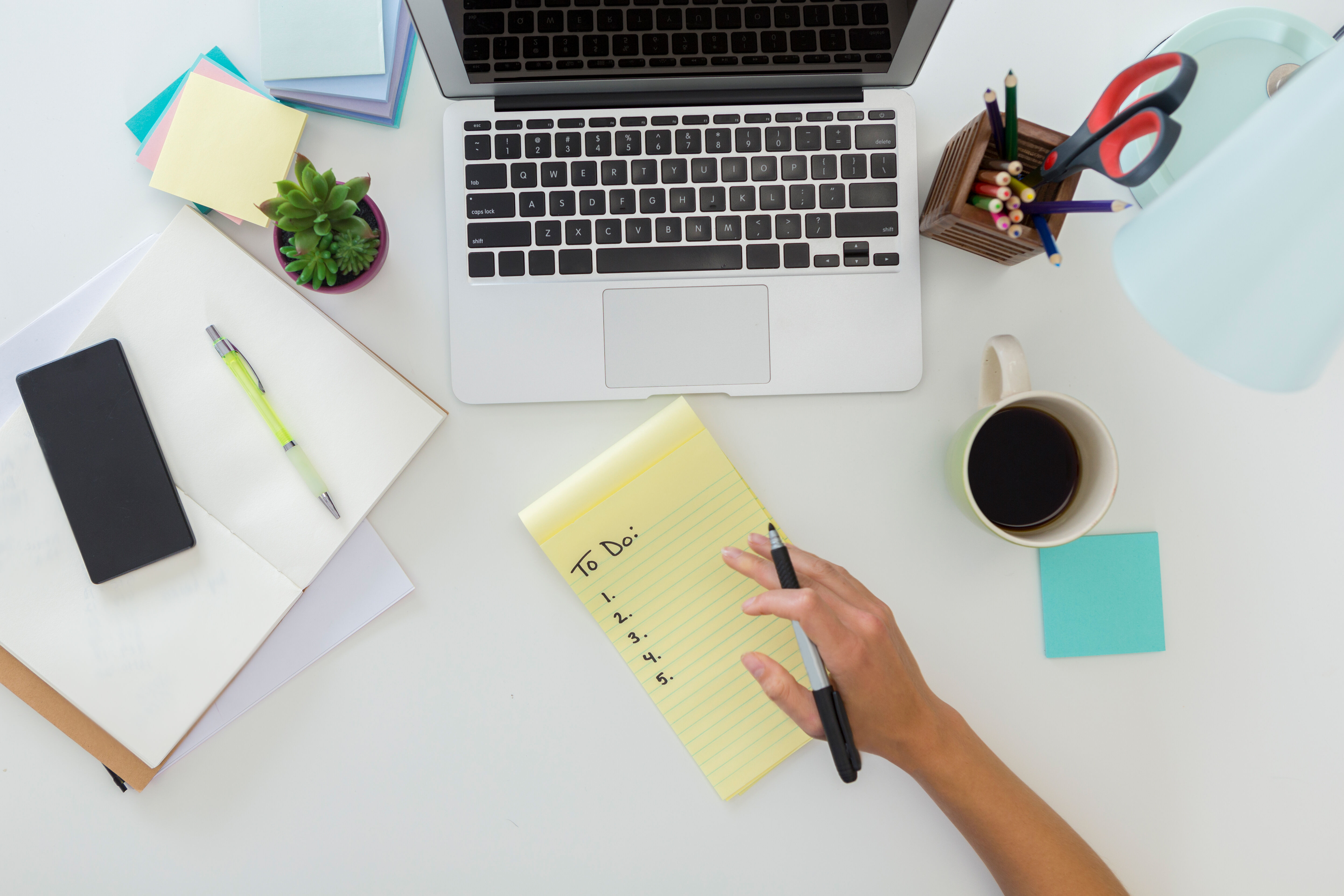 Bird's eye view of human hand writing to do list on home office desk