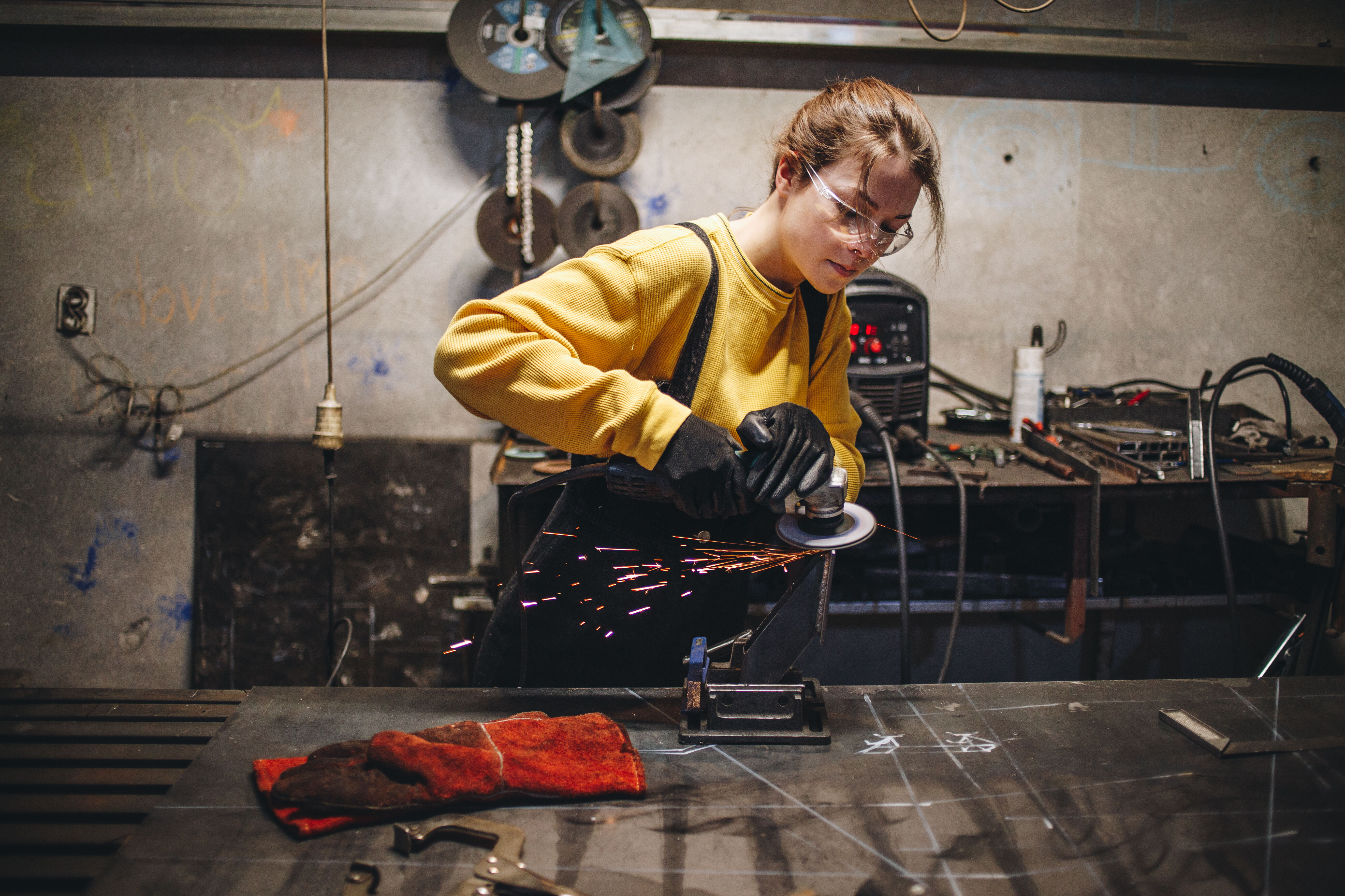 Young female working at a metal workshop, grinding metal with grinder.